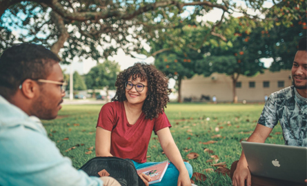 three young people sitting on the grass talking