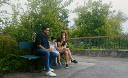 a family with a young son sits on a bench in a park