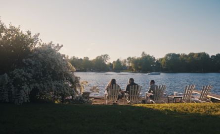 three people in Muskoka chairs sit beside a beautiful waterway
