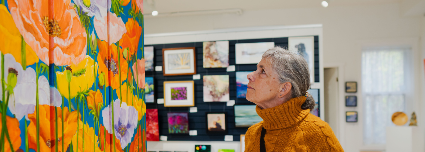 a woman in an orange sweater looks at paintings