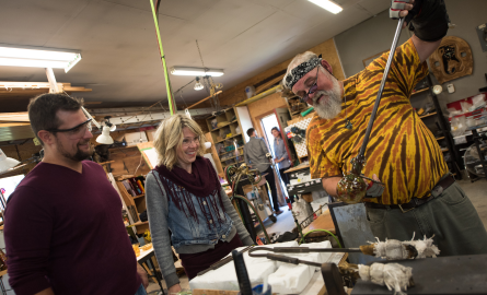 a man creating blown glass while visitors watch