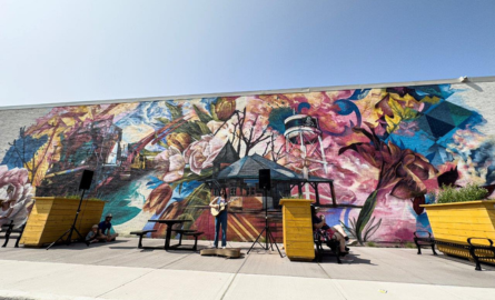 a woman sings in front of a colourful mural