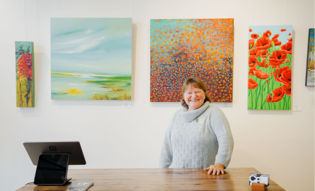 a woman stands proudly behind a service counter in front of a wall of beautiful paintings