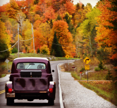a vintage car driving down a country road in the fall